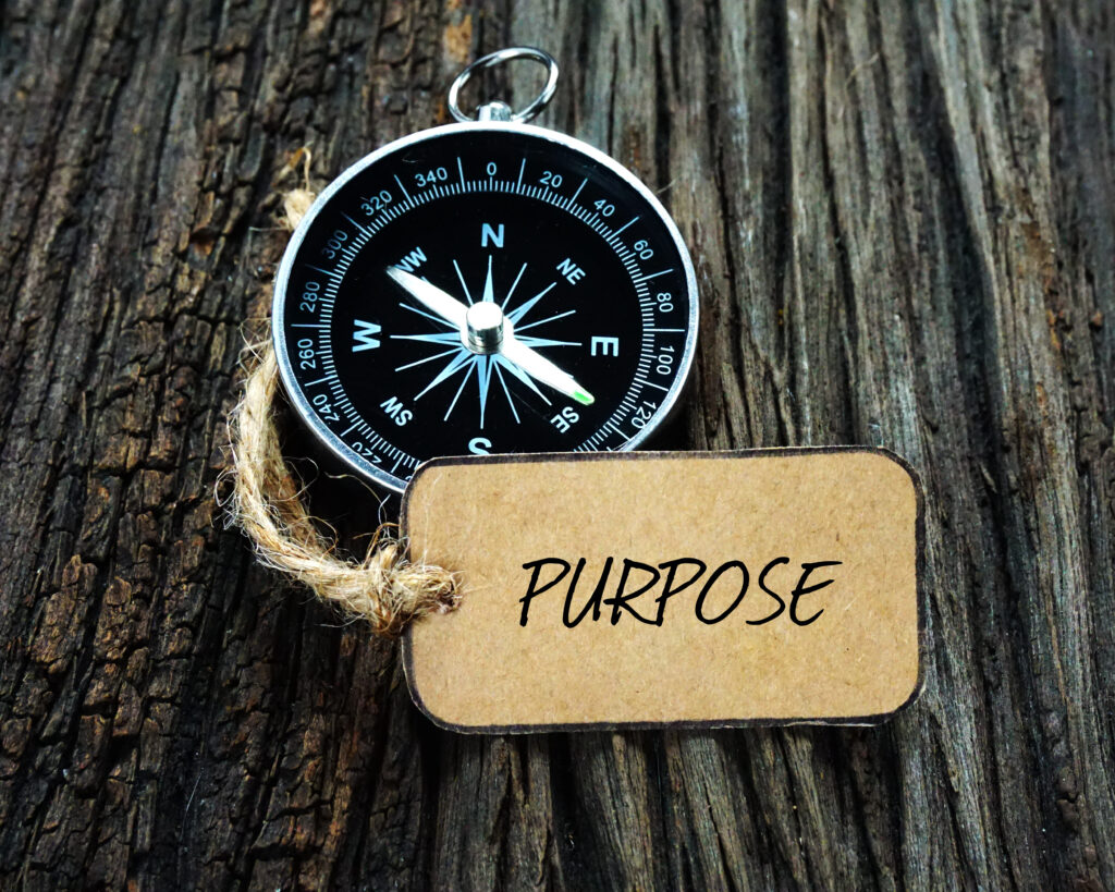 Compass and paper tag written with PURPOSE on wooden background.